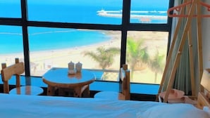 A room with a large window overlooking a beach, a bed, a small round table with cups, and a wooden chair. - Zhuhai Wailingding Island Wanghaige (Beach Swimming Area) (Zhuhai)