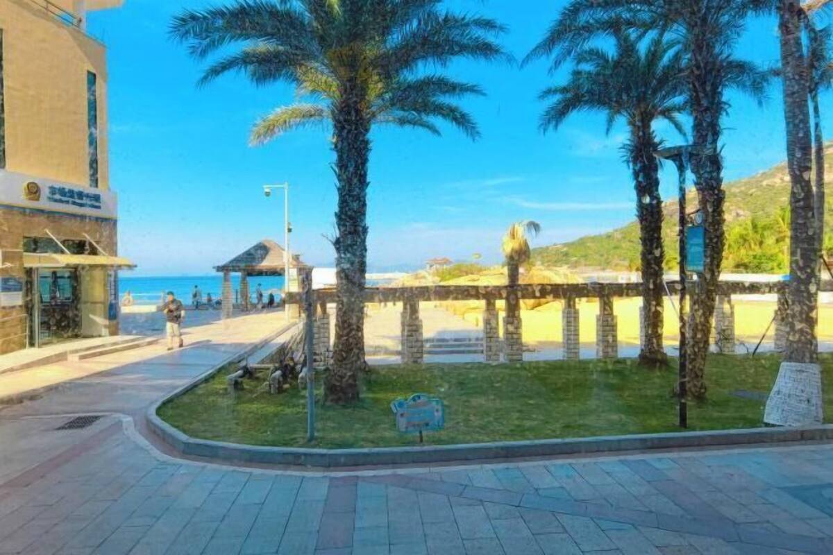 A beachfront area with palm trees, a beach, and a building with a sign.