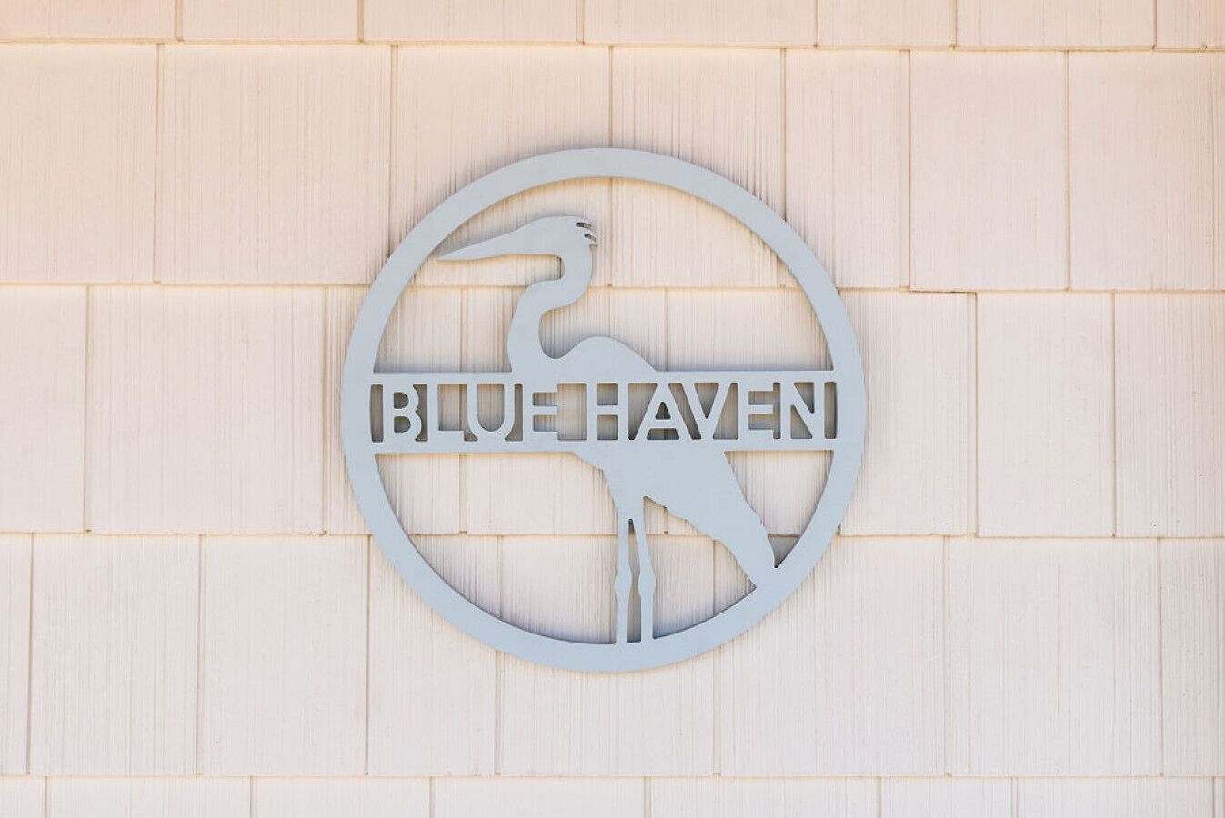 A circular sign with a bird silhouette and the text "BLUE HAVEN" on a light wooden wall.
