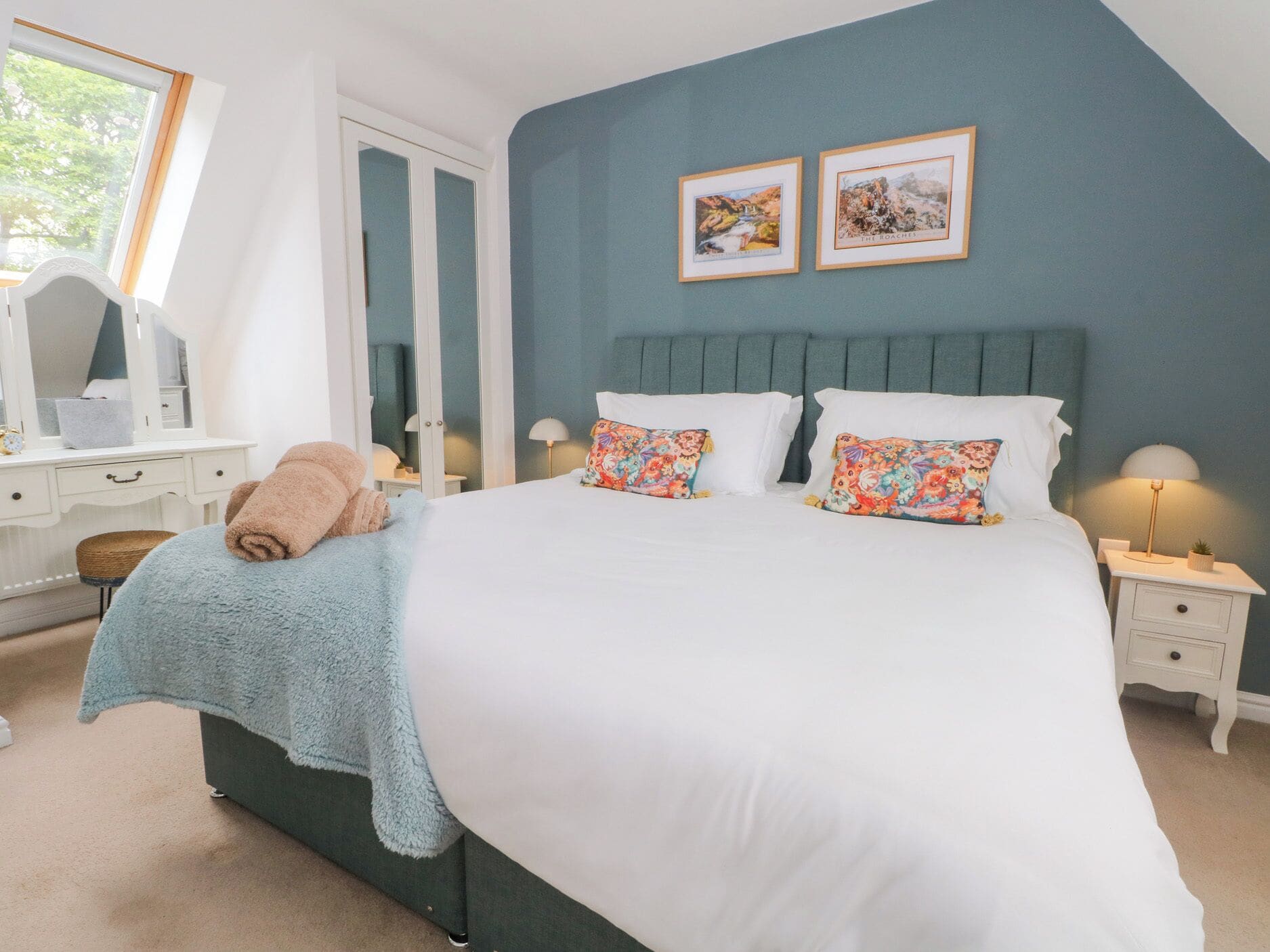 A bedroom with a large bed, two side tables, a dresser, and a window.