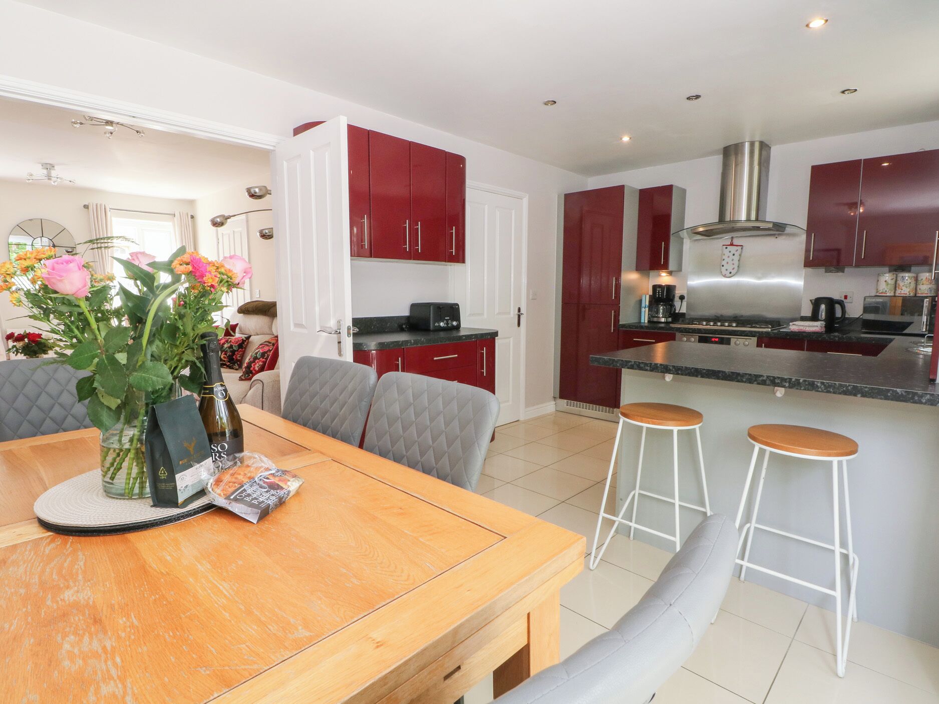 A modern kitchen with red cabinets, a central island, and a dining area with a wooden table and grey upholstered chairs.