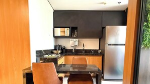 Une cuisine moderne avec un plan de travail noir, des appareils en acier inoxydable et des meubles de rangement en bois. On y trouve une table à manger avec deux chaises.