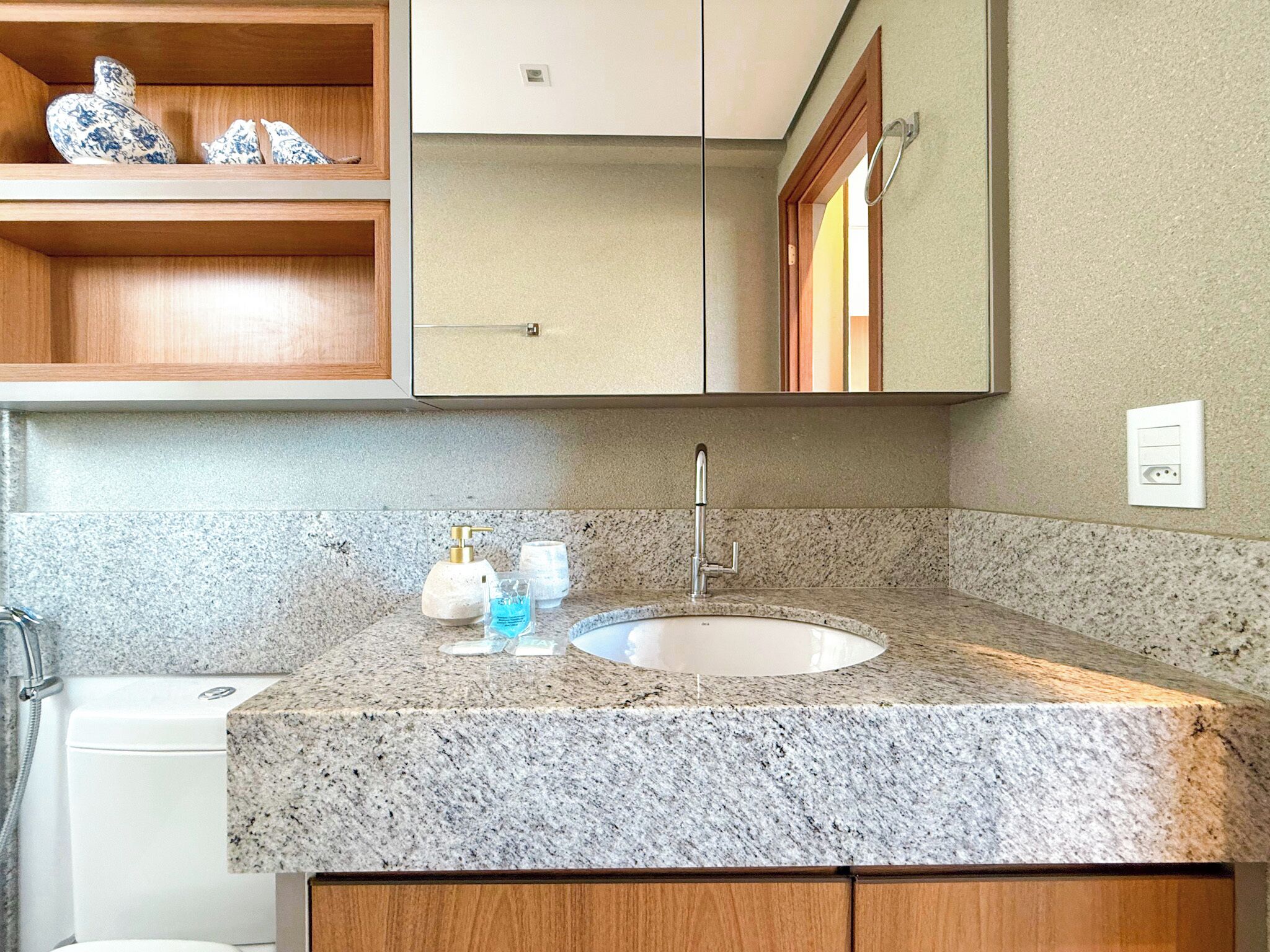 A bathroom with a granite countertop, a sink, a mirror, and wooden cabinets.