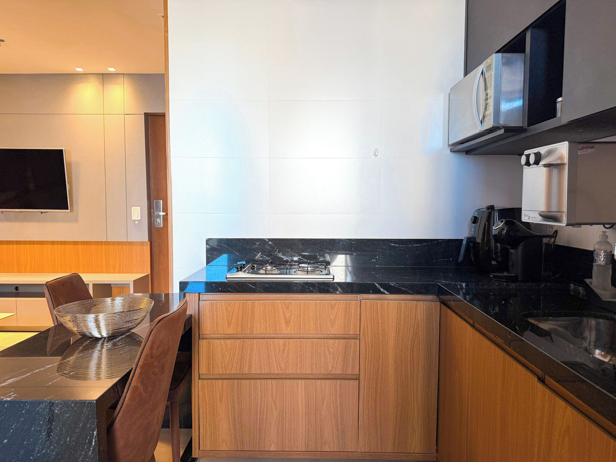 Una cocina moderna con encimera de mármol negro, armarios de madera, estufa integrada, microondas y cafetera.