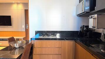Una cocina moderna con encimera de mármol negro, armarios de madera, estufa integrada, microondas y cafetera.