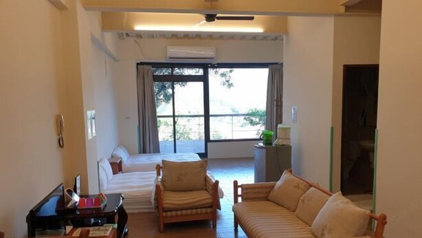 A room with a bed, two sofas, a small table, and a window with curtains. - Sanyi Happiness Bed and Breakfasts (Miaoli)