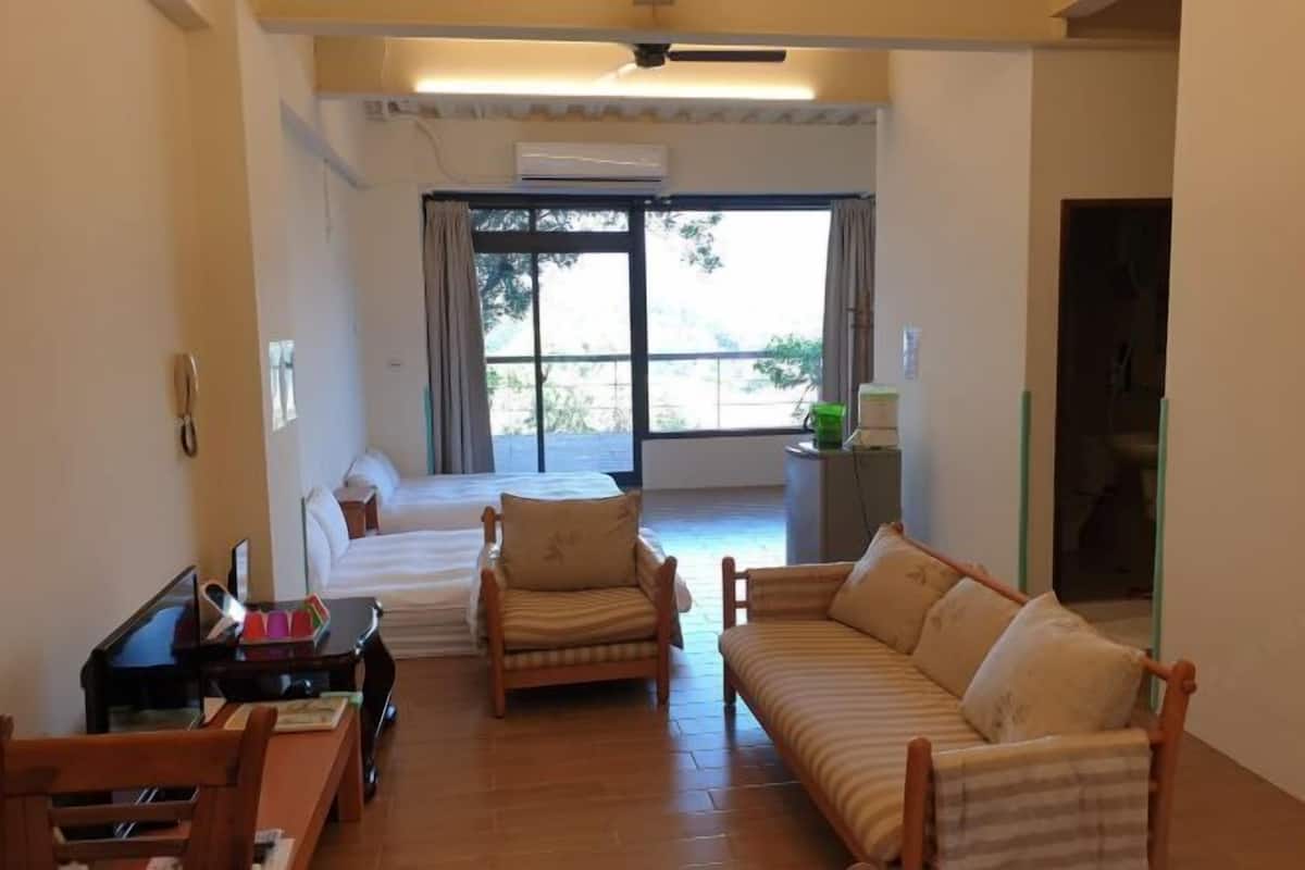Una habitación con cama, dos sofás, una mesita y una ventana con cortinas.