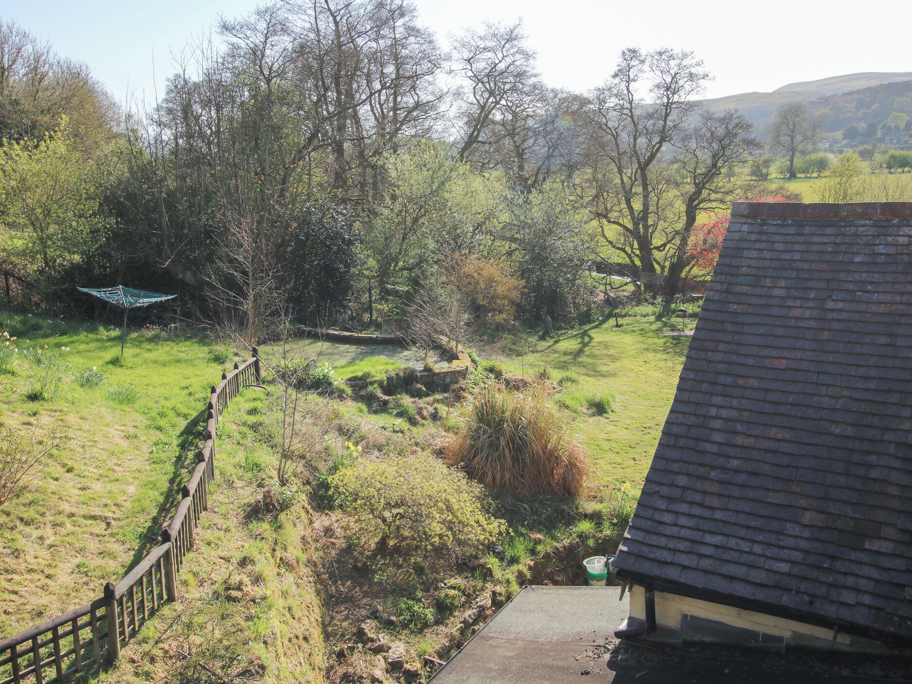 A rural landscape with a wooden fence, a grassy field, and a house with a dark roof.