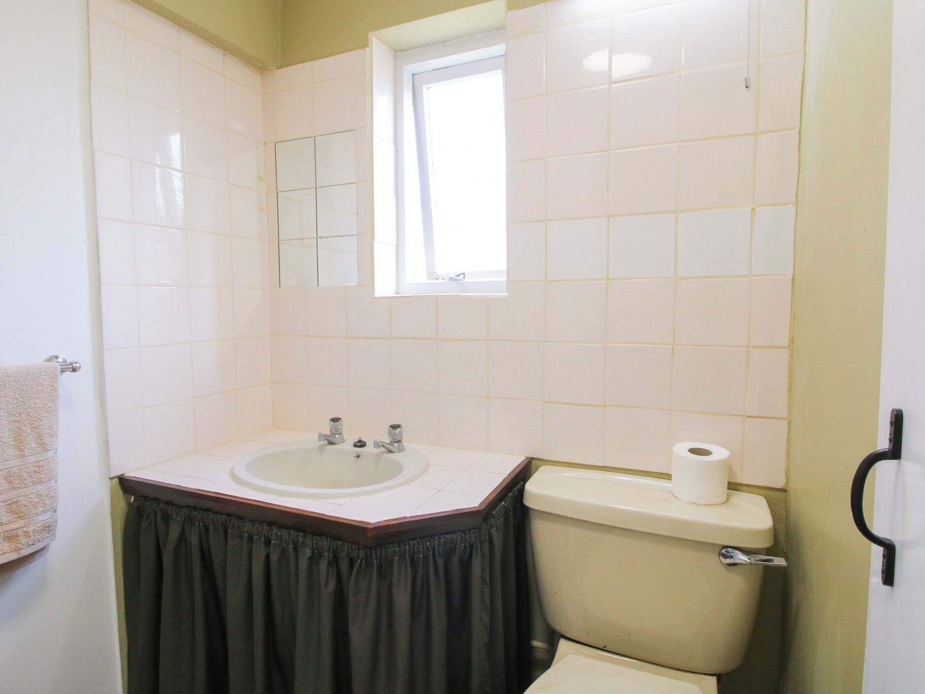 Une salle de bain avec un lavabo blanc, un miroir, des toilettes et une fenêtre.
