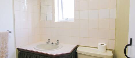 Une salle de bain avec un lavabo blanc, un miroir, des toilettes et une fenêtre.