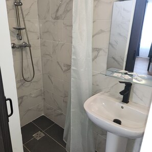 A bathroom with a shower, a sink, and a glass shelf. - Hotel de l'Europe Pantin (Pantin)