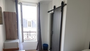 Un dormitorio con una cama, un escritorio, una silla, un armario y una ventana con cortinas.