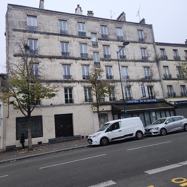 A multi-story building with a sign for "HOTEL D'EUROPE" indicating it is a hotel. There are several parked cars in front, and a tree is visible on the sidewalk. - Hotel de l'Europe Pantin (Pantin)