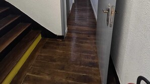 Un pasillo estrecho con suelo de madera y una puerta a la derecha.