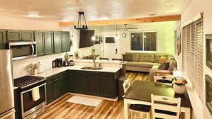 A modern kitchen with green cabinets, a stainless steel stove, and a dining area with a table and chairs.
