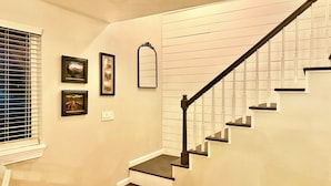 A staircase with white railings and dark steps, leading to a landing with a light switch and framed pictures on the wall.
