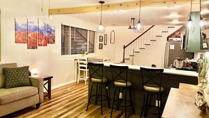 A modern kitchen with wooden flooring, a bar area with stools, a dining table with chairs, and a staircase leading to another level.
