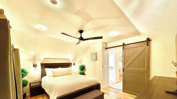 A bedroom with a bed, a ceiling fan, a sliding door, and a bench.