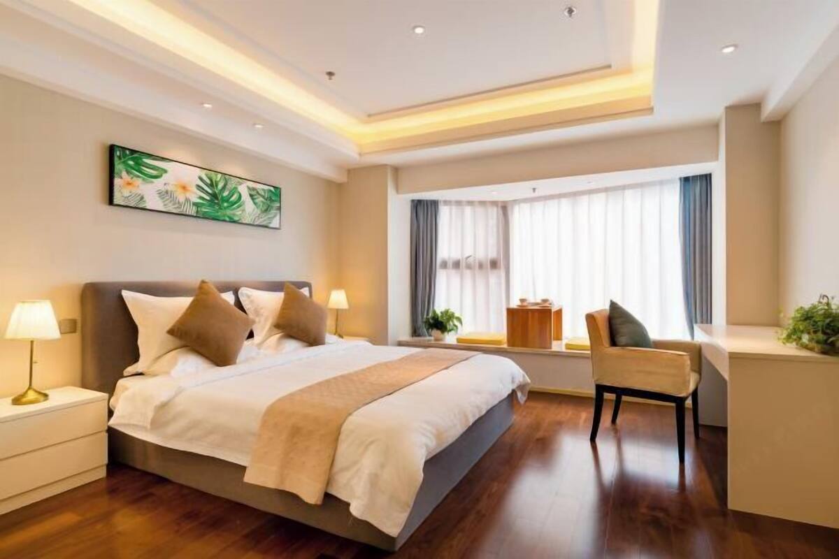 Ein modernes Hotelzimmer mit einem großen Bett, Nachttischlampen, einem Schreibtisch und einem fenster mit Vorhängen.