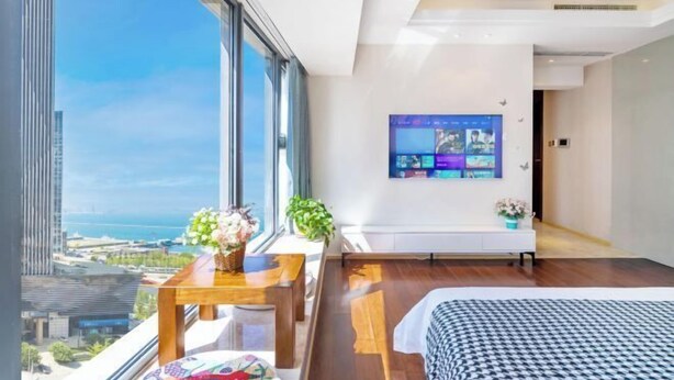 A modern hotel room with a large window, a bed, a small table, and a mounted TV. - Zhanyou Home Sea View Apartment Hotel(Dalian Venice the City of Water) (Dalian)