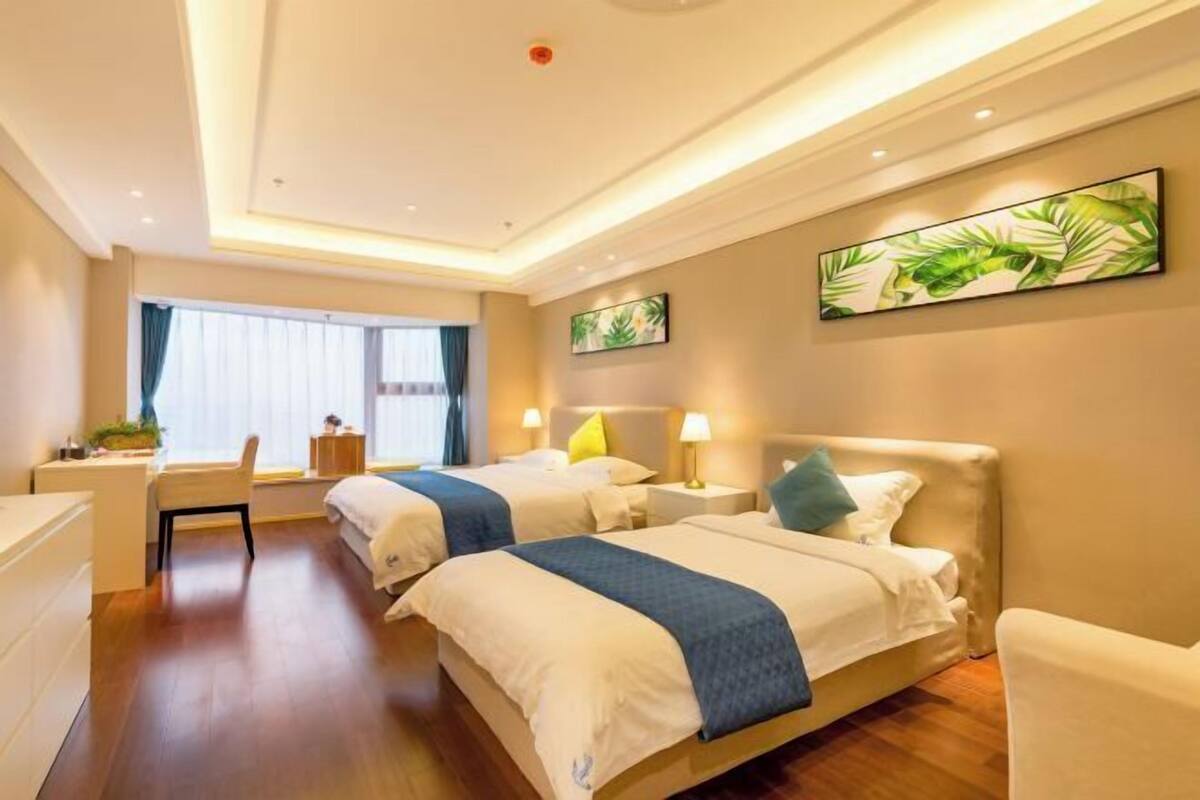Ein Hotelzimmer mit zwei Betten, einem Schreibtisch, einem Stuhl und einem großen Fenster mit Vorhängen.