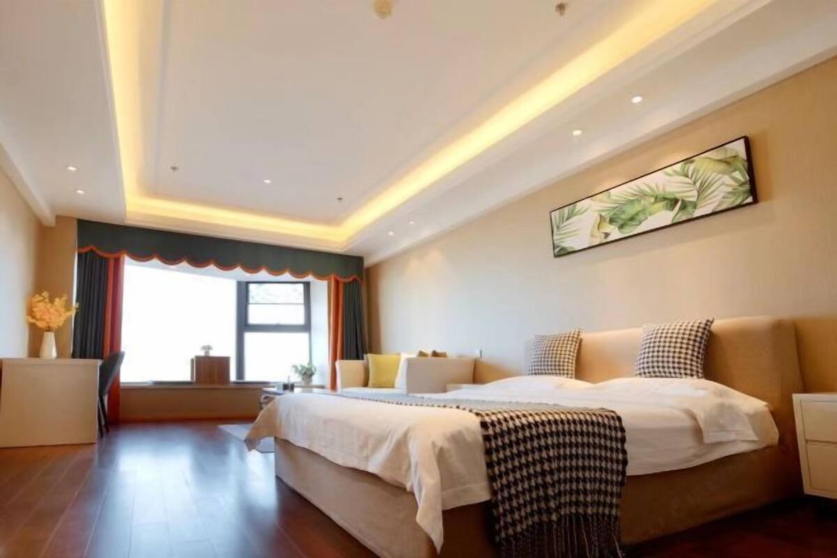 Ein Hotelzimmer mit einem großen Bett, Nachttischen, einem Schreibtisch und einem Fenster mit Vorhängen.