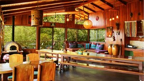 A rustic wooden interior with a large dining table, benches, and a cozy seating area with cushions. - Finca Camino Nuevo#4 -Ecolodge, Sea & Forest Views (Monteverde)