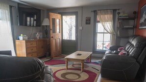 Una sala de estar con un sofá, una mesa de centro y una alfombra. Hay un mueble de madera y un televisor en la pared.