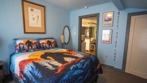 Un dormitorio con una cama grande, un cuadro enmarcado en la pared, un espejo y una puerta que da a otra habitación.