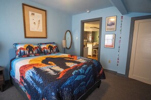 Cozy retreat with a large bed and nature-inspired quilt, featuring a framed certificate and mirror.
