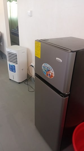 A refrigerator with a sticker, a white air cooler, and a red bucket.