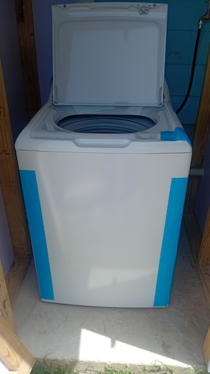 A white and blue washing machine in a small room with wooden walls and a concrete floor.