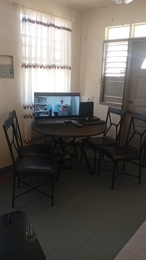 A dining area with a round table, four chairs, a television, and a window with curtains.