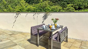 An outdoor dining area with wicker furniture and a glass table, surrounded by stone tiles and a low wall. - Lavender Cottage -UK49209 (near Okehampton)
