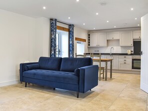 A modern living room with a sofa, a dining table, and a kitchen area.