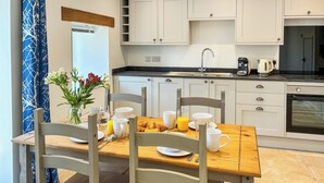 A modern kitchen with white cabinets, a wooden dining table, chairs, and a breakfast setting. - Lavender Cottage -UK49209 (near Okehampton)