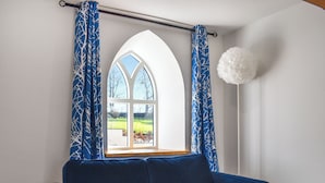 A room with a blue sofa, a window with a white frame, and blue curtains with a tree pattern. - Lavender Cottage -UK49209 (near Okehampton)