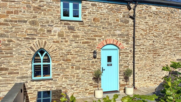 A stone building with a blue door, arched windows, and a small sign indicating a cottage. - Lavender Cottage -UK49209 (near Okehampton)