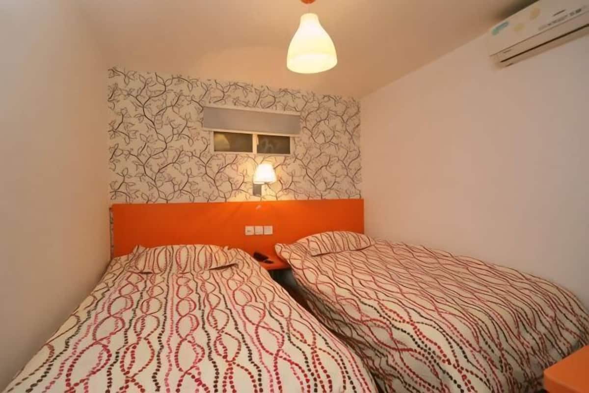 A room with two beds, a wall-mounted air conditioner, and a window with a light fixture.