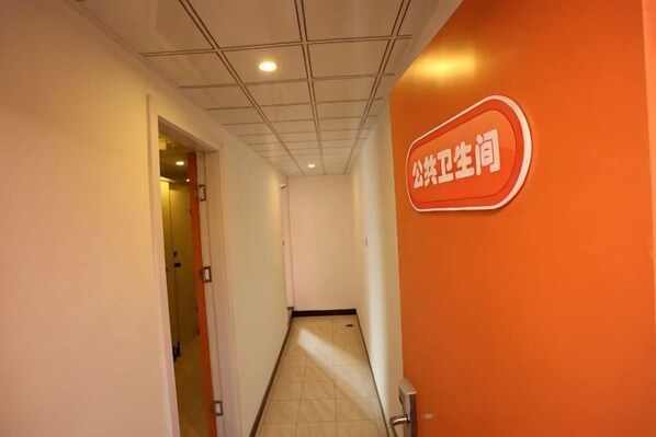 A corridor with a tiled ceiling, a sign on the right wall, and a door at the end.