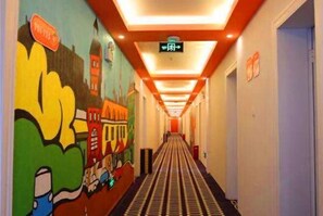 A hotel hallway with a mural on the left, a ceiling with recessed lighting, and a sign indicating an exit. - Pod Inn Hotel (Shanghai Wusong International Cruise) (Shanghai)