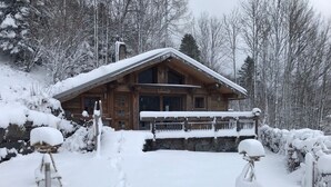 A wooden lodge with a stone foundation, a wooden porch, and a sign that reads "Le Colibri."