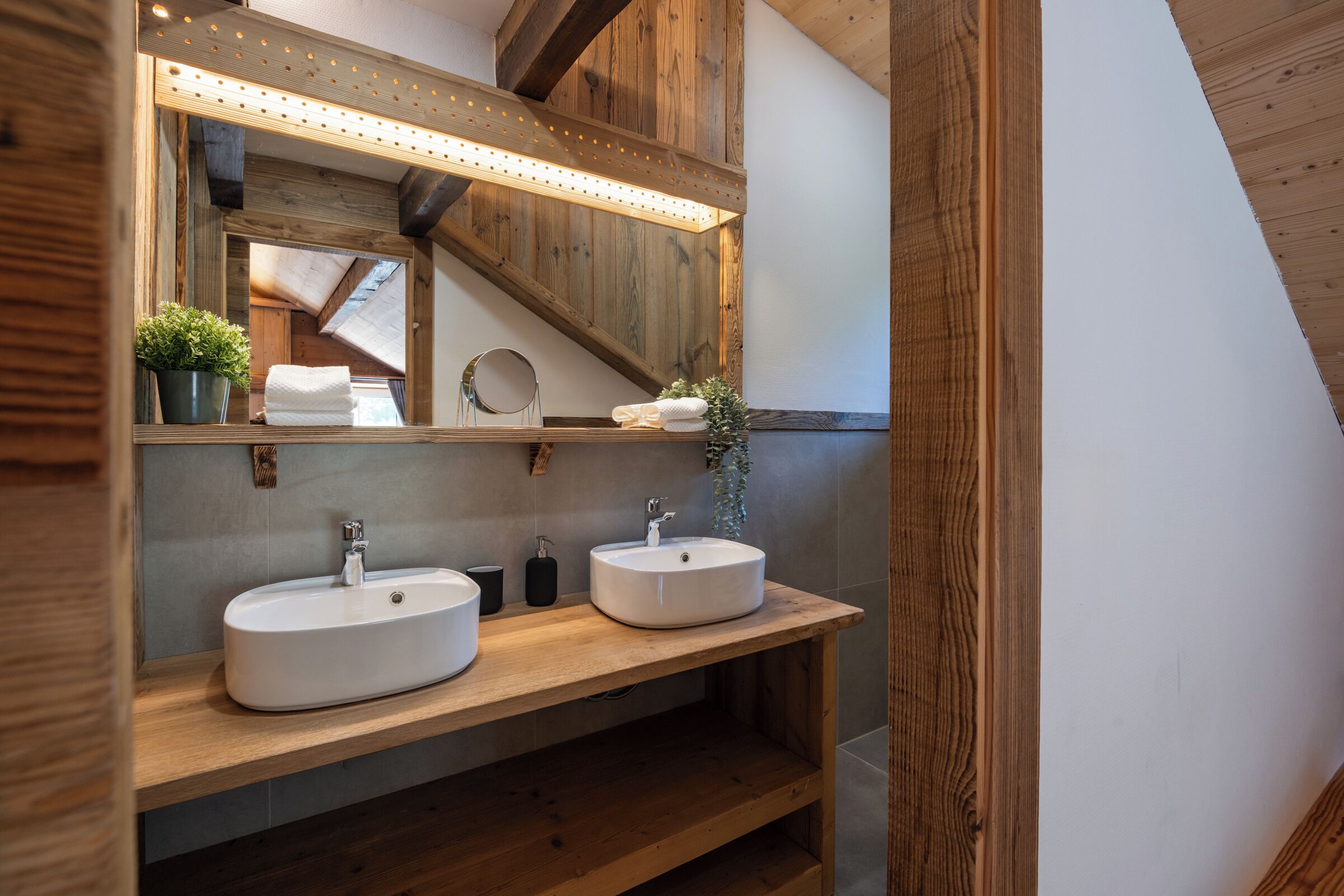 A bathroom with two sinks, a mirror, and a wooden shelf.