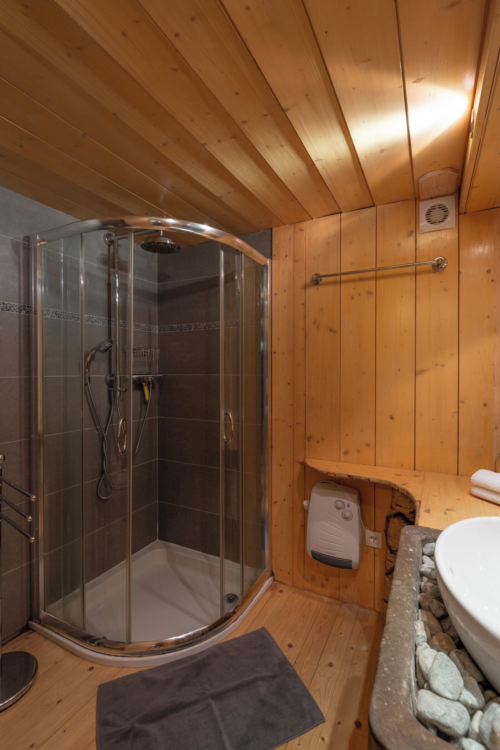 A wooden cabin bathroom with a glass-enclosed shower, a built-in sink with a stone basin, and a towel rack.
