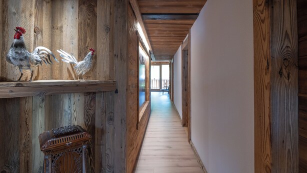 A wooden hallway with rustic decor, including wall-mounted roosters and a carved wooden bench.