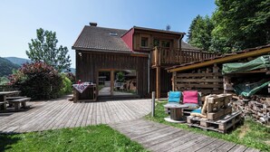 A wooden cabin with a deck, a covered outdoor seating area, and a view of the surrounding landscape.