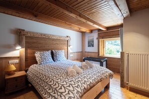 Quarto com estrutura de madeira, cama, mesas de cabeceira, janela e radiador.