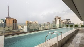 Una piscina en la azotea con vistas a un paisaje urbano, que incluye una torre de comunicaciones y edificios modernos.
