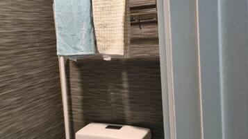 A bathroom with a toilet, a towel rack with two towels, and a green cleaning brush.