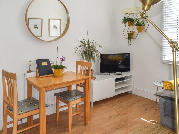 A modern living room with a wooden dining table, two chairs, a TV, and a small side table with a lamp. - 2 bedroom accommodation in Ventnor (Ventnor)